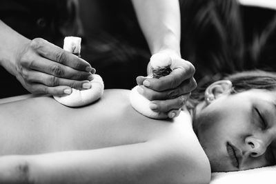 Hands of an ayurveda massage therapist pressing herbal bolus bags onto clients skin