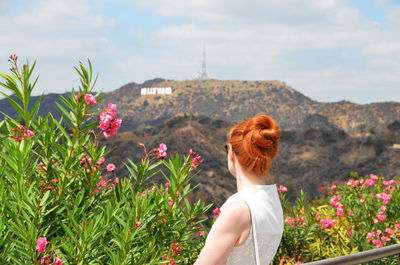 Woman looking at hollywood hills against sky while standing by pink flowers