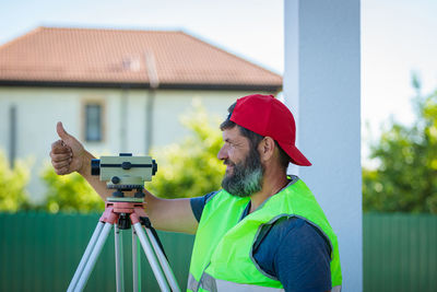 Rear view of man photographing with camera while standing against building