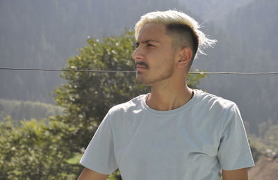 A south asian young guy with dyed white hair looking sideways while posing outdoor with copy space