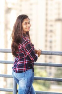 Portrait of young woman standing against railing