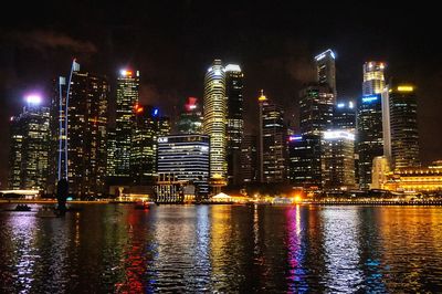 Illuminated buildings by river against sky at night