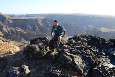 Full length of man sitting on rock against sky