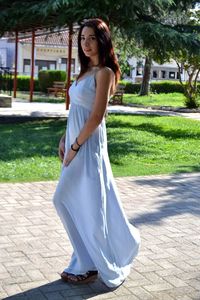 Portrait of young woman wearing white gown while standing on footpath