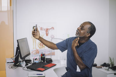 Male otolaryngologist doing online consultation through video call on smart phone while sitting at desk in clinic