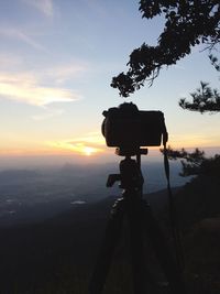 Silhouette photographing camera on landscape against sky during sunset