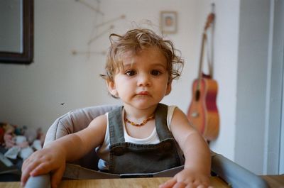 Baby sat at dining table in high chair wearing dungarees 