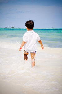 Little boy walking on the beach watching the caribbean ocean