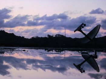 Silhouette birds flying over lake against sky during sunset