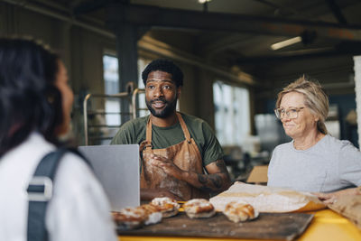 Male and female owners talking with customer buying bread at bakery