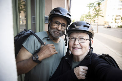 Smiling senior couple taking selfie with cycling helmet outside house