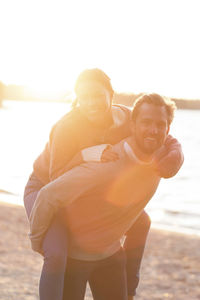 Portrait of affectionate couple enjoying piggyback ride on beach during sunset