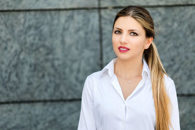 Portrait of young businesswoman standing against wall