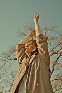 Full length of woman standing by bare tree against sky