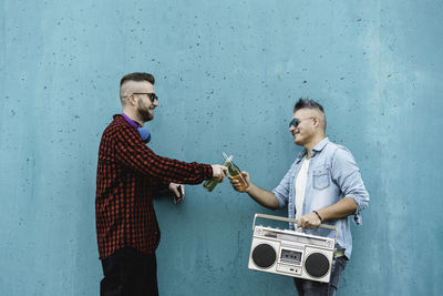 Men toasting bottles while standing with radio against wall