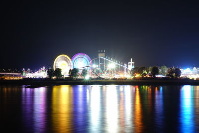 Illuminated city by river against sky at night