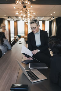 Mature businesswoman discussing over document with female colleague at conference table in board room