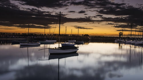 Sailboats moored at harbor during sunset