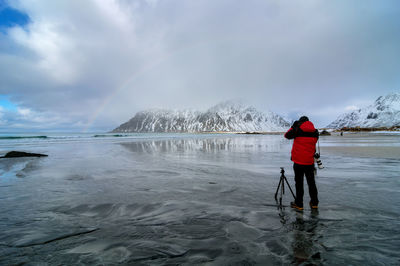 Full length of man photographing rainbow while standing at beach against sky