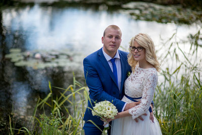 Portrait of newlywed couple standing against pond