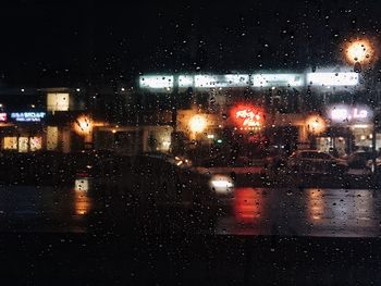 Illuminated city seen through wet glass window at night