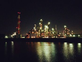 Illuminated factory by river against sky at night