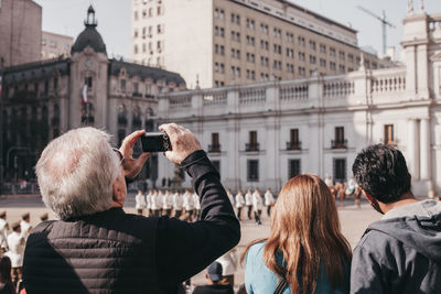 Rear view of people photographing buildings in city