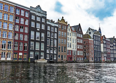 Buildings by canal against sky in city