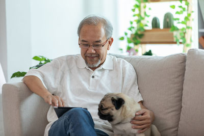 Cheerful man using digital tablet while sitting with dog on sofa