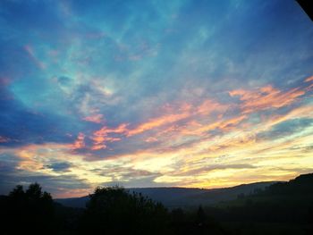 Silhouette trees against dramatic sky during sunset