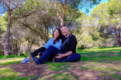 Happy woman sitting in park against trees