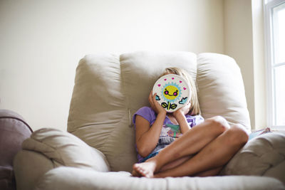 Girl holding toy against her face while sitting on couch against wall