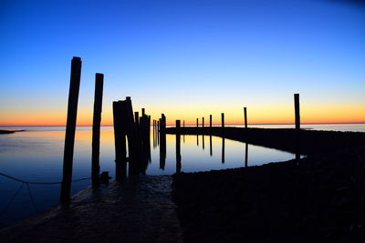 Silhouette wooden posts in sea against clear sky