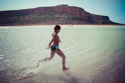 Full length of shirtless boy at beach against sky