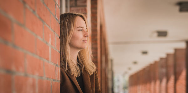 Young woman looking away while standing by brick wall