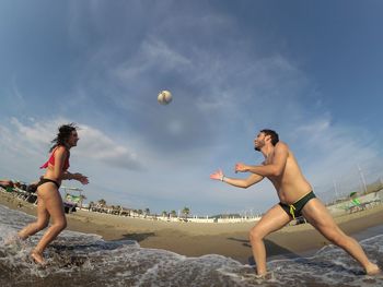 Low angle view of couple playing with ball at beach