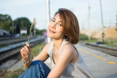 Portrait of woman holding plant while sitting against sky