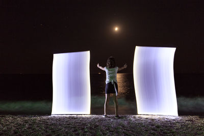 Woman standing with light painting at beach against sky