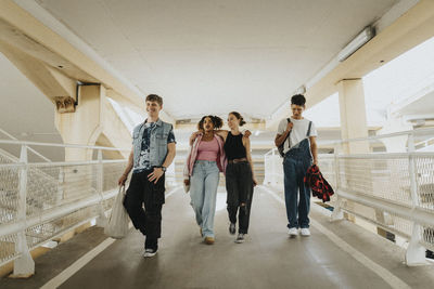 Happy young fashionable male and female friends walking on footpath of parking garage