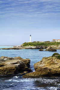 Lighthouse amidst sea and buildings against sky