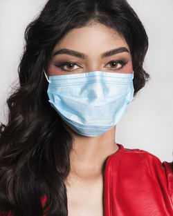 Portrait of beautiful young woman wearing mask over white background