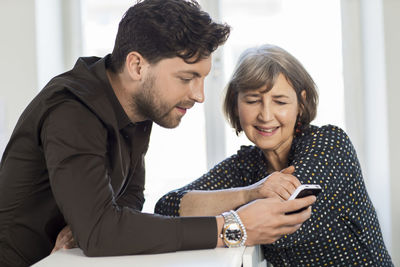 Young man and mature woman looking at phone in office