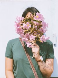 Woman holding pink flowers over face against wall