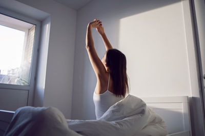 Woman in a white t-shirt is sit on the bed under the blanket in the room im morning