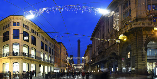 People on illuminated street amidst buildings at night