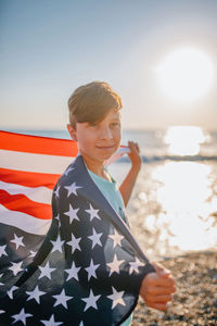 Boy holding american flag at beach against sky