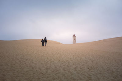 People on sand dune in desert against sky