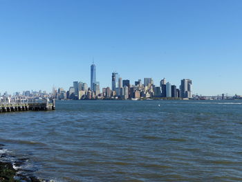 Sea in front of cityscape against clear blue sky