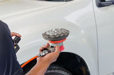 Cropped image of mechanic holding polishing equipment against car