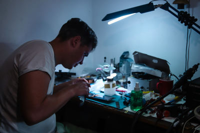 A man carefully repairing a phone screen in a workshop. the phone is disassembled, with tools 